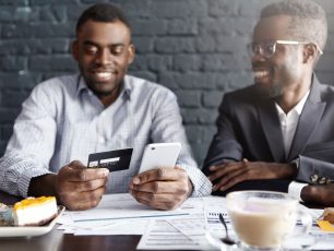 two men sitting at a table looking at a cell phone.